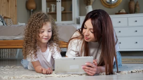 Morena mamá y niña jugar juego en línea en tableta blanca — Vídeos de Stock