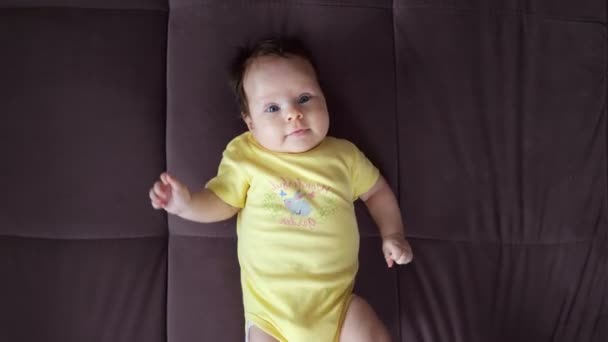 Vacker baby i gul body suit ligger på soffan — Stockvideo