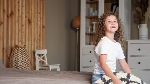 Boldog fiatal óvodás lány esik nagy szürke ágy — Stock videók