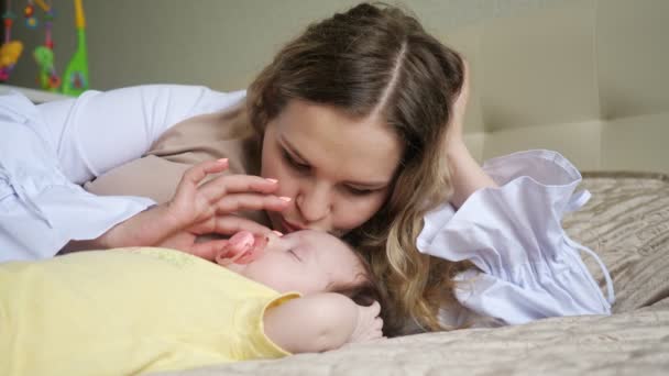 Giovane madre culla e bacia il bambino con un ciuccio sdraiato sul letto, rallentatore — Video Stock