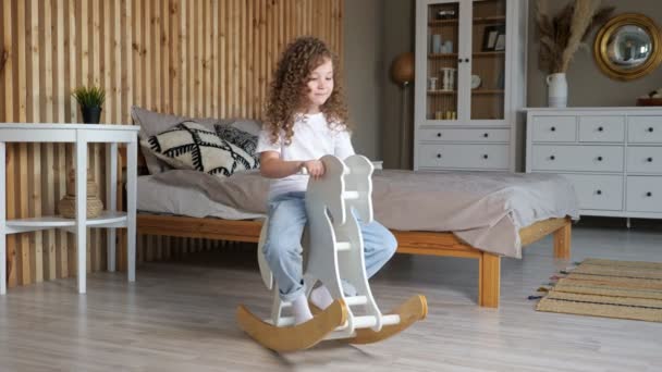 Preschooler girl with curly hair sits on rocking horse — Stock Video