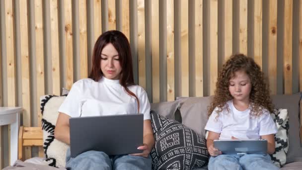 Concentrated woman with laptop and daughter with tablet — Stock Video