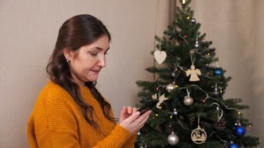 Yılbaşı ağacının arka planında telefonu olan genç bir kadının yan görüntüsü