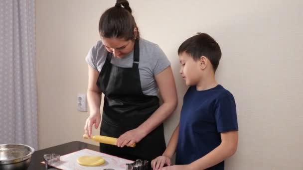Jeune femme déploie la pâte avec un rouleau à pâtisserie, un garçon avec des emporte-pièces se tient à côté — Video