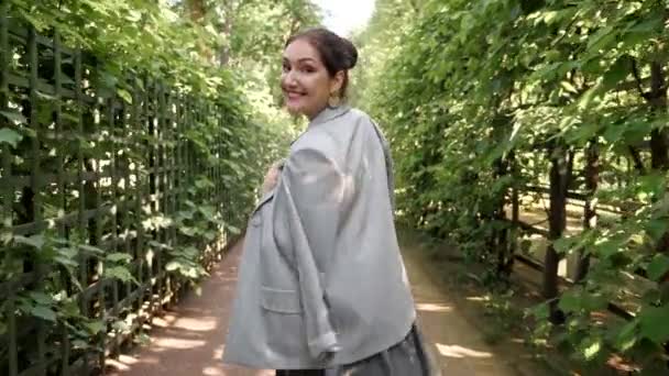 年轻的黑发女人穿过花园，转过身来，面带微笑 — 图库视频影像