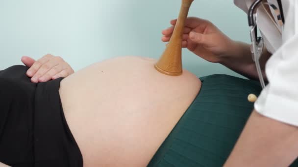 Gynekolog naslouchá těhotné ženě s fetoskopem na klinice — Stock video