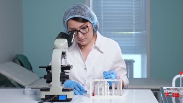 Asistente de laboratorio concentrado mira en el microscopio en la mesa — Vídeo de stock