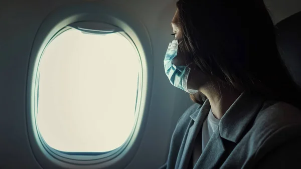 Kobieta w masce medycznej siedzi przy oknie samolotu — Zdjęcie stockowe