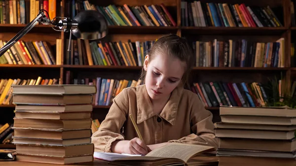 Aburrido colegiala mira en el libro y escribe en copybook — Foto de Stock