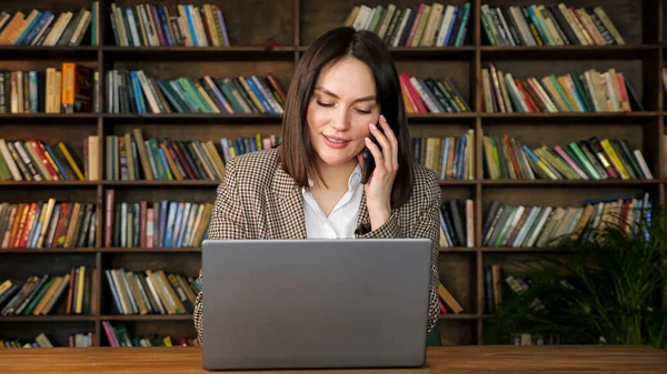 Ung affärskvinna talar på svart telefon i bibliotekshallen — Stockfoto