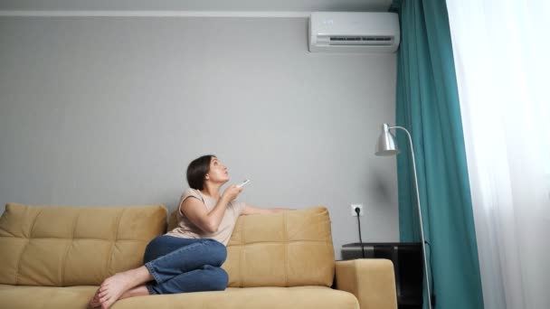Mujer ajusta el aire acondicionado mientras está sentado en el sofá, cámara lenta — Vídeos de Stock
