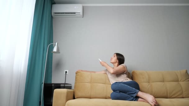 Brünette Frau schaltet die Klimaanlage ein, während sie auf der Couch sitzt — Stockvideo