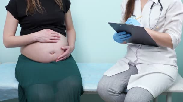 Arzt mit Klemmbrett untersucht schwangere Patientin auf Couch — Stockvideo