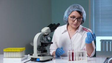 Kadın laboratuardaki test tüplerindeki kan örneklerini kontrol ediyor.