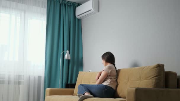 Zijaanzicht van een brunette vrouw past de airconditioner terwijl zitten op de bank — Stockvideo