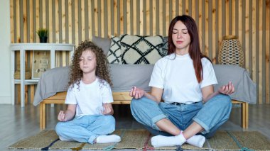 Saçları dökülmüş küçük bir kız ve annesi yoga pozlarında oturuyor.
