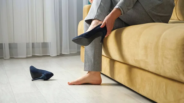 Неузнаваемая женщина сидит на диване и снимает туфли на высоком каблуке — стоковое фото