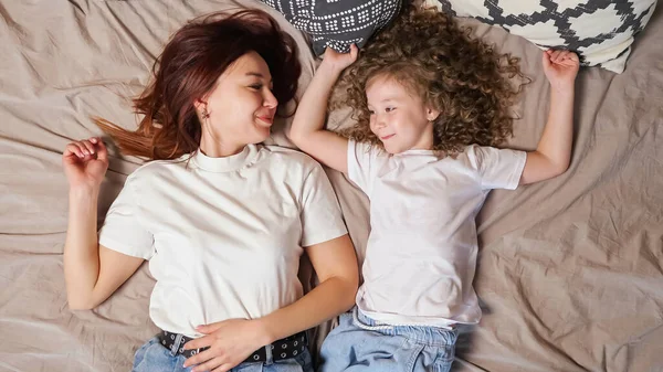 Расслабленная мать и дочка лежат на серой кровати — стоковое фото