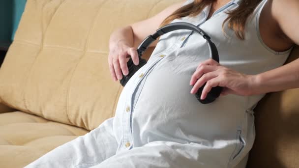 Unrecognizable pregnant woman puts headphones on belly — Stock Video