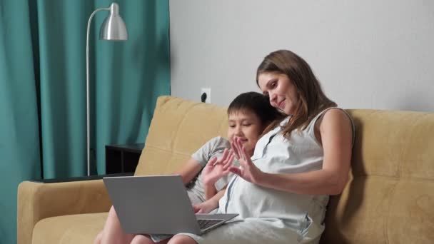 Pregnant woman and boy talking by video call on laptop while sitting on couch, slow motion — Stock Video