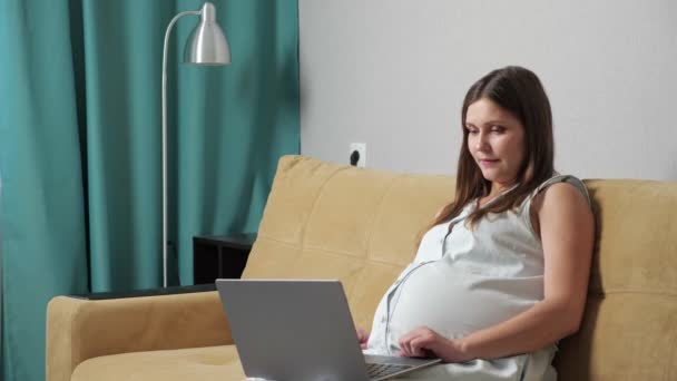 Pregnant woman talking on video call on laptop while sitting on sofa — Stock Video