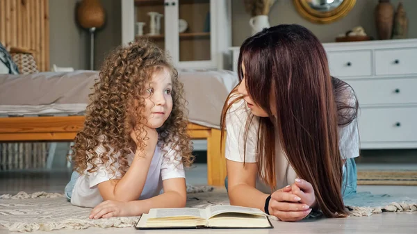 Улыбающаяся мама читает сказки дошкольнице на полу — стоковое фото