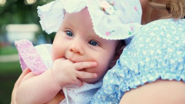 Mavi gözlü küçük kız annesinin kollarında oturuyor.