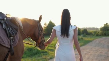 Beyaz elbiseli esmer kadın kahverengi atıyla geziyor.