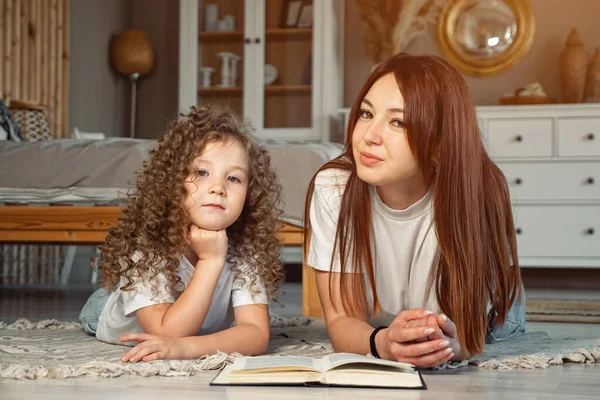 Улыбающаяся мама и дочка с книгой смотрят в камеру — стоковое фото