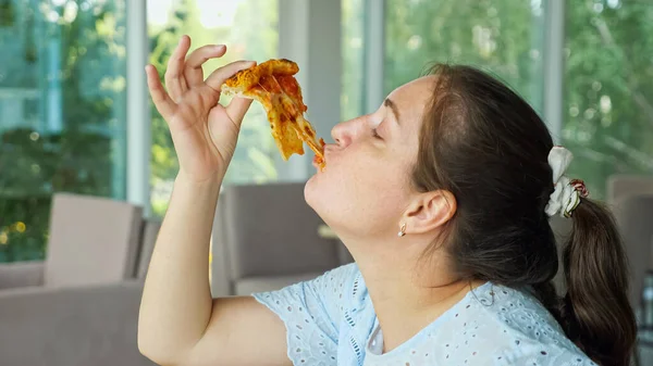 Mulher pega um pedaço de pizza e come com prazer — Fotografia de Stock