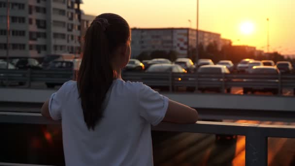 Jeune écolière avec queue de cheval regarde coucher de soleil sur le pont — Video