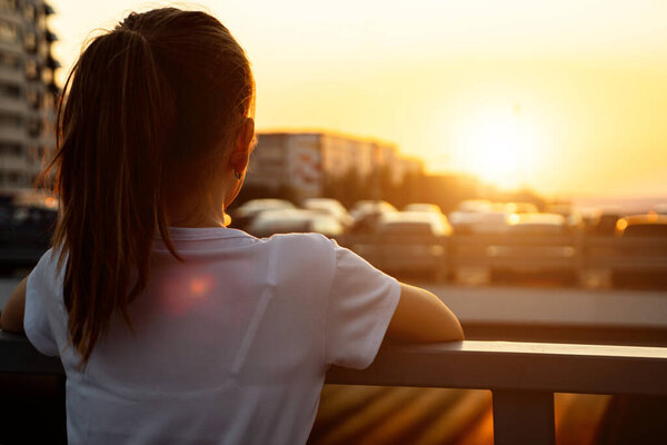 Schoolgirl at back sunset. Teenage girl blonde with long hair in ponytail admires setting sun light and blurry city buildings close backside view