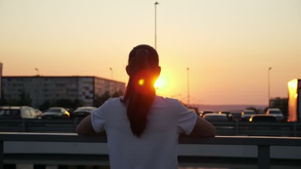 Remaja gadis dengan rambut poni mengagumi pengaturan matahari dan kota — Stok Video