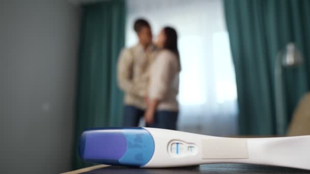 Κοντινό πλάνο του θετικού τεστ εγκυμοσύνης με ευτυχισμένο ζευγάρι στο παρασκήνιο — Αρχείο Βίντεο