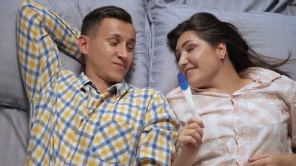 Άντρας και γυναίκα μιλάνε ενώ ξαπλώνουν στο κρεβάτι συζητώντας για τεστ εγκυμοσύνης, top view — Αρχείο Βίντεο