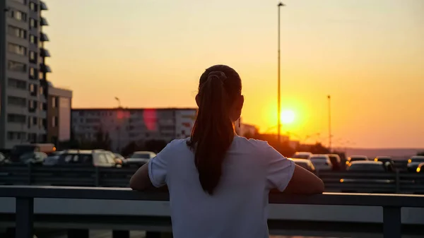 Young schoolgirl with ponytail looks at sunset on bridge — Stock Photo, Image