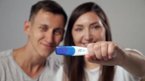 Close-up do teste de gravidez positivo no fundo turvo do homem e da mulher felizes, câmera lenta — Vídeo de Stock