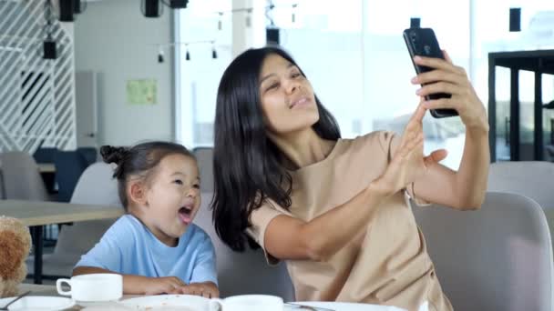 Joven madre sostiene el teléfono inteligente y hace selfie con su hija — Vídeos de Stock