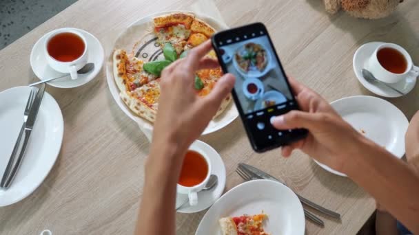 Młoda kobieta trzyma czarny smartfon i robi zdjęcia pizzy — Wideo stockowe