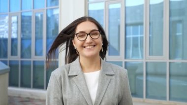 Takım elbiseli, gözlüklü, sokaklarda yürüyen mutlu bir kadın.