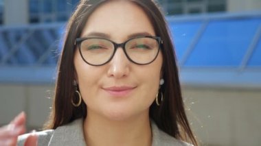 Gözlüklerini düzelten ve kameraya gülümseyen genç bir kadının yakın çekimi.
