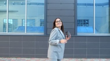 Gözlüklü bir kadın ve sokakta dans eden bir fincan kahveli bir takım elbise.