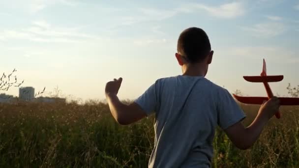 Chico corre a través del campo y juega con un pequeño avión al atardecer, cámara lenta — Vídeos de Stock