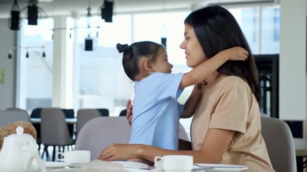 Giovane bambina abbraccia la mamma con il sorriso vicino al tavolo nel caffè — Video Stock