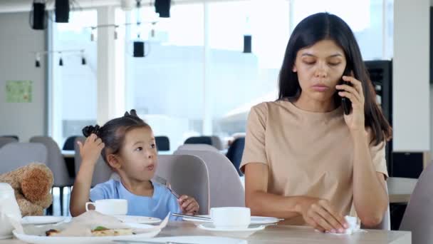 Zakenvrouw reinigt kind mond praten op smartphone in cafe — Stockvideo