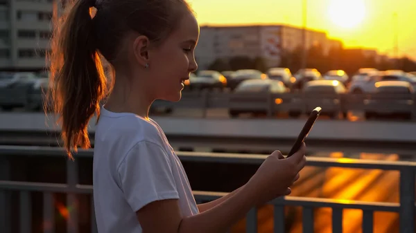 Lány típusok okostelefon és pózol szelfi naplementekor — Stock Fotó