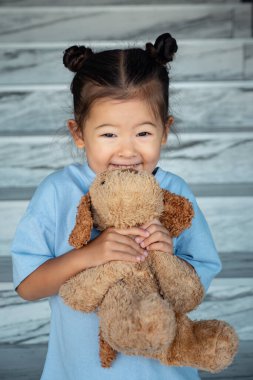 Mavi tişörtlü küçük kız kahverengi köpek oyuncağı tutuyor.