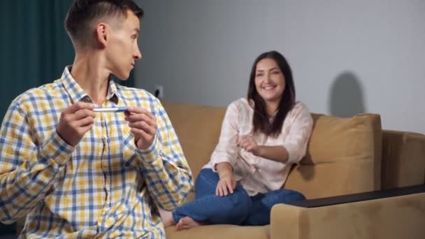 Un hombre joven con una prueba de embarazo mira hacia atrás a la mujer feliz. felicidad de la próxima paternidad — Vídeo de stock