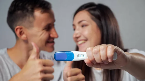 Primer plano de la prueba de embarazo positiva en el fondo borroso de hombre y mujer felices — Foto de Stock