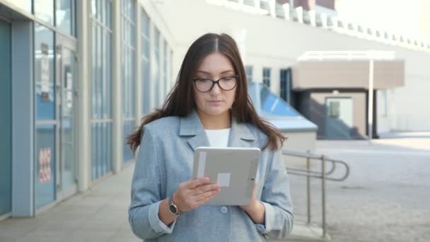 Junge Frau im formellen Anzug und Brille blickt auf der Straße in eine Tablette, Zeitlupe — Stockvideo